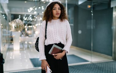  Çekici kıvırcık saçlı, 20 'li yaşlarda, şık giyinmiş, alışveriş merkezinde boş vakit geçiren Afro-Amerikan kadını.