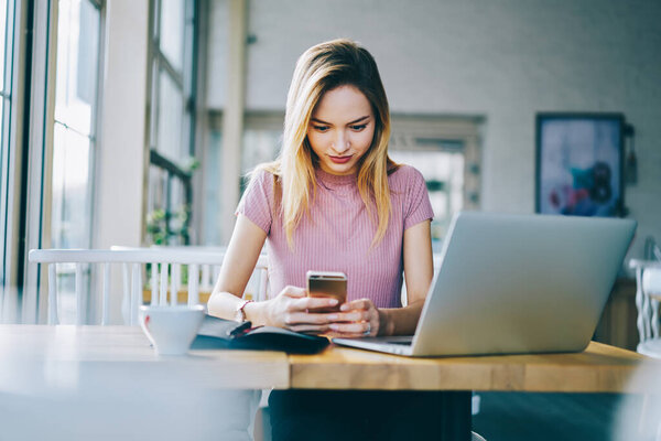 Millennial hipster girl watching video publication on modern smartphone technology using internet connection in coffee shop