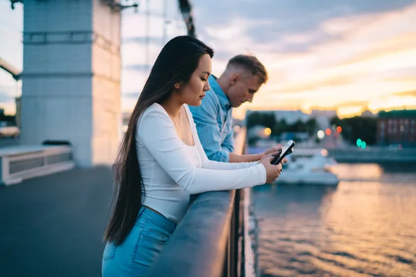 Male and female bloggers using cellphone gadget during date time at urban bridge ignoring live communication,