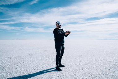 Miğferli sakallı bir adam, kurumuş gölün üzerinde duruyor ve tatil boyunca sanal gözlüklerle manzaranın tadını çıkarıyor.