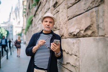 Yaşlı beyaz erkek turistin emeklilik tatilleri sırasında cep telefonu cihazıyla yarım boy portresi.