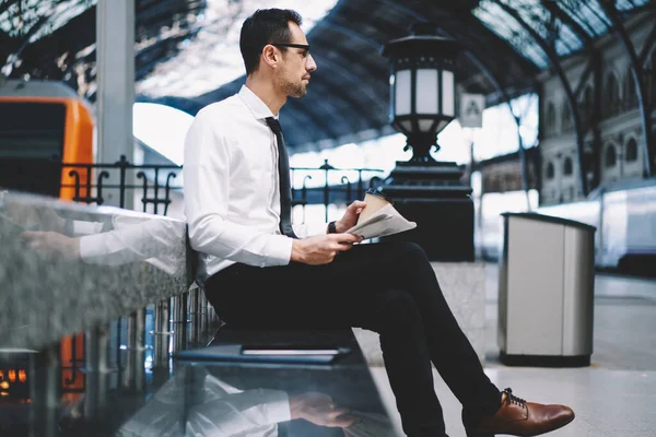 Pensive businessman spending morning routine with mass-media and coffee to go while waiting for railway