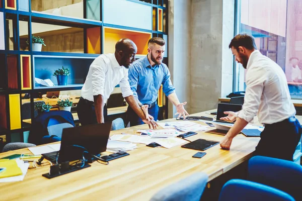 Frustrated worried office worker in formal clothes working on startup gesturing explaining partners problem of project standing in modern office room