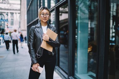 Milenyum blogcusunun yarım boy portresi. Elinde eğitim çizim defteri var. Müzik podcast 'i dinlerken kameraya bakıyor.