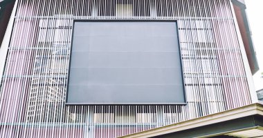 Geometrik tasarım ve şehir caddesinde gündüz vakti merkezde boş ilan panosu bulunan fütüristik binanın düşük açılı dış görünümü