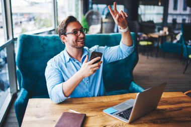 Gülümseyen profesyonel serbest yazar internetteki iş için modern cihazlar kullanarak kablosuz bağlantının şifresini öğrenmek için garsonu arıyor. Başarılı iş adamı öğle yemeğinde kafede servis edilmeyi bekliyor.