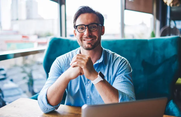 Portrait of handsome freelancer satisfied with completing online project successfully made great work, prosperous businessman in eyewear using laptop computer for distance job sitting in coffee shop