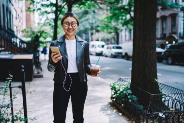 Şehrin boş zamanlarında kameraya gülümseyen optik gözlüklü ve modern kulaklıklı neşeli hippi kız portresi.