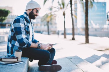 Moda giyinmiş erkek turist web sitesi gezisi yayınları okumak için şehir merdivenlerinde dinleniyor kahve ve eğitim ekipmanlarıyla