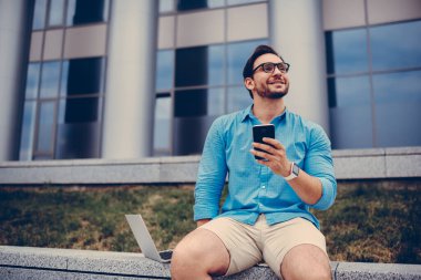 Moda gözlüklü mutlu hippi hafta sonları plan yapıyor ve cep telefonu uygulaması üzerinden internetten bilet alıyor.,