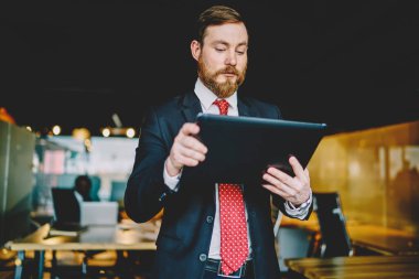 Katı siyah takım elbiseli ciddi sakallı iş adamı. Beyaz gömlek, kırmızı kravat. Tablette kırmızı sörf yapıyor.