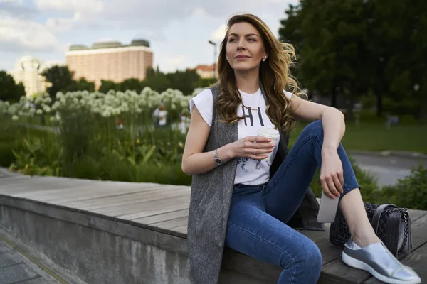 Pondering woman with caffeiene beverage and mobile phone thinking about weekend leisure spending