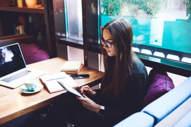 Kafeteryada sörf yaparken dizüstü bilgisayarı ve bir fincan kahveyle masaya oturan odaklanmış serbest çalışan kadın.