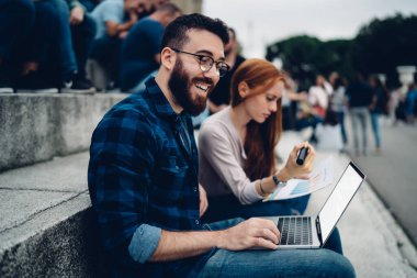 Neşeli hipster çocuk dizüstü bilgisayardan olumlu video izliyor ve en iyi arkadaşıyla beyin fırtınası yaparken gülüyor.