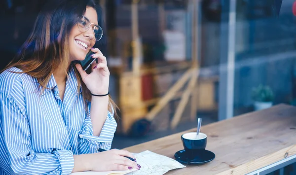 喫茶店で携帯電話で会話をするコーヒーを飲みながらテーブルに座っている女性の笑顔のガラスを通して — ストック写真