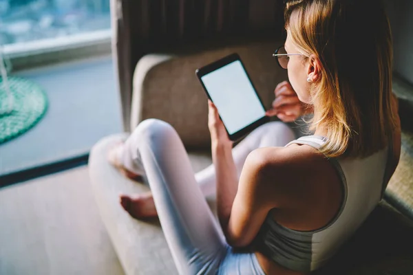身着白色运动服 双腿交叉坐在沙发上 在公寓平板电脑上观看视频的年轻女性的背影 — 图库照片