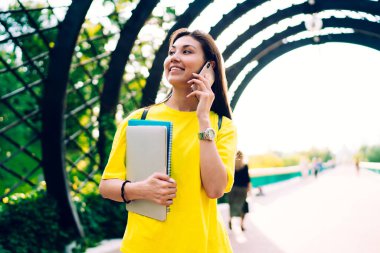 Not defteri ve tabletle mutlu genç bir bayan telefonda konuşurken ve sabah gezintisinde dekoratif kemer altında haberleri tartışırken gülümsüyor ve yüzünü çeviriyor.