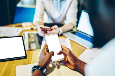 Yukarıdan gelen çok ırklı akıllı iş adamları cep telefonlarında sörf yapıyor ve masada dizüstü bilgisayar ve tabletle çalışan bilgileri arıyorlar.