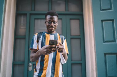 Görme düzeltmesi için klasik gözlüklü mutlu Afrikalı Amerikalı hipster modern cep telefonu cihazında GPS uygulaması üzerinden GPS 'i takip ediyor.