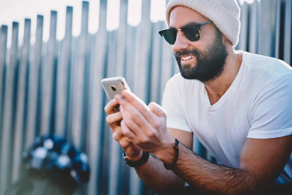 流行のサングラスや冬の帽子で中東の男性は 銀行アプリケーションを閲覧し アカウントの詳細を確認するためにスマートフォンガジェットを使用して — ストック写真
