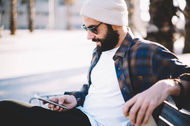 Güneş gözlüklü ve modaya uygun şapka kontrollü Orta Doğulu erkek blogcu şehirde boş zamanlarında 4g internet kullanarak e-posta aldı