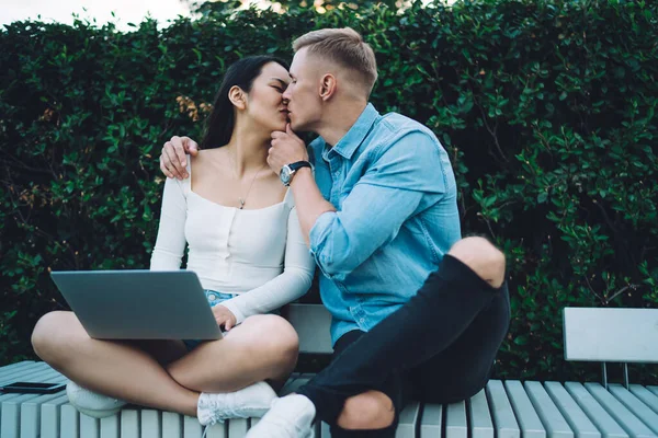 情侣情投意合在自由职业项目上与现代笔记本电脑坐在长椅上接吻 — 图库照片