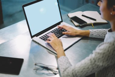 Yukarıdan bakıldığında tanınmayan bir kadın modern çalışma alanında masada oturuyor ve modern aletler kullanarak yeni bir proje üzerinde çalışıyor.