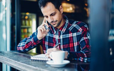 Yakışıklı, şık gömlekli, ders kitabına göre bilgi yazan ve partnerini konuşmaya çağıran bir adam.