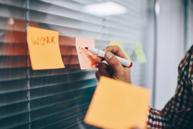 Tanımlanamayan erkek cam duvarın yanında duruyor ve ofiste sıradan gömlekler giyerken çıkartma üzerine notlar yazmak için elinde kırmızı işaret kullanıyor.