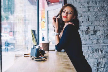 Kendine güveni olan, koyu mavi elbiseli, tahta masada elinde retro fotoğraf makinesiyle duran genç bir kadının yan görüntüsü.
