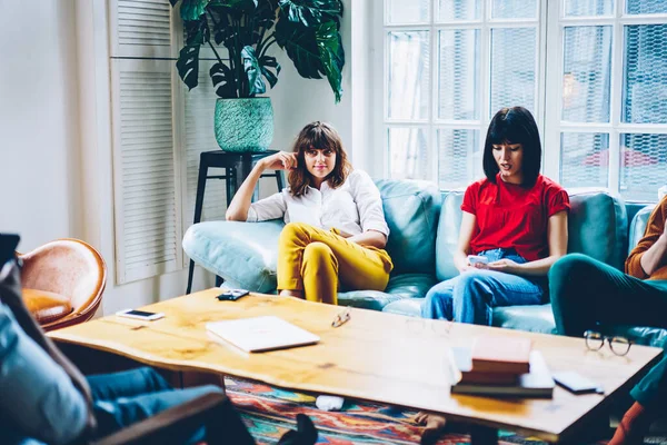 时尚的年轻女性在舒适的客厅里 用智能手机 坐在女性朋友旁边的沙发上 安安静静地呆在家里 — 图库照片