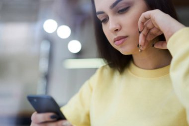 Güzel esmer, 20 'li yaşlarda elinde cep telefonu ile sosyal ağlardan haberleri okuyan bir kadın.