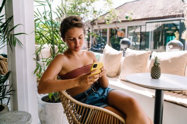 Kot şortlu, beyaz koltuğun yanında oturan ve Phuket 'te tatil yaparken akıllı telefondan mesaj atan bir kadın.