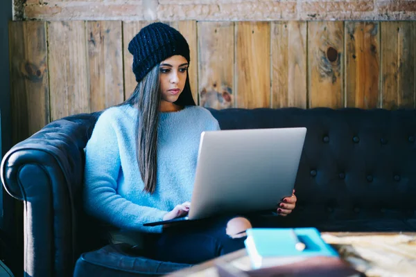 Caucasian freelancer in stylish hat searching web page for browsing publication and create content during distance job on laptop