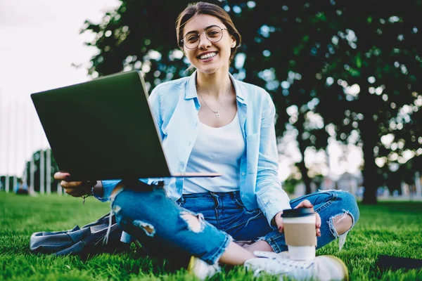 快乐的嬉皮士女孩 带着外卖咖啡杯 在公园里用上网本和网络连接对着摄像机微笑 — 图库照片