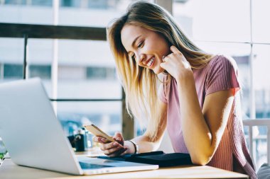 Modern akıllı telefon teknolojisi üzerine video yayınını izleyen mutlu hippi kız kahve dükkanında internet bağlantısı kullanıyor.