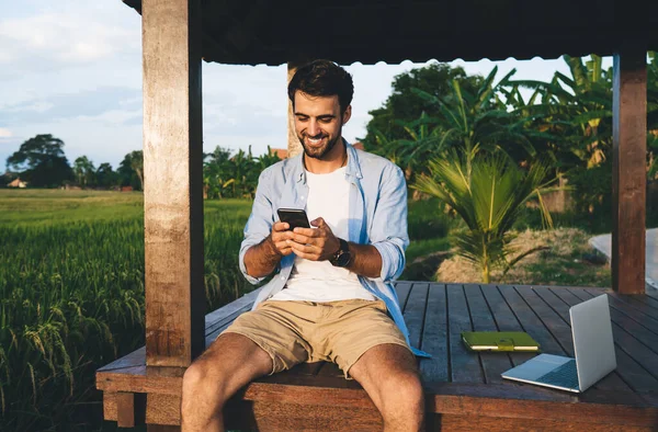Pozytywny Mężczyzna Zarostem Stroju Letnim Patrząc Ekran Smartfona Uśmiechnięty Podczas — Zdjęcie stockowe
