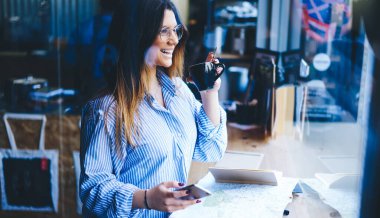 Kafeteryada boş vakit geçiren, bir fincan kahve ve akıllı telefonla masaya bakan mutlu gülen bir kadının yan görüntüsü.