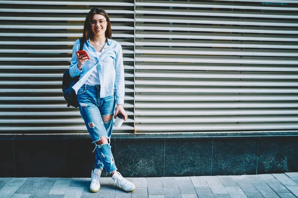 Portrait of happy woman in optical eyewear and stylish apparel smiling at camera and posing at urban setting