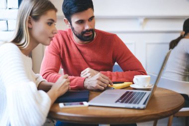 Sakallı ciddi bir adam ve açık kafeteryadaki kahve masasında otururken ekrana bakıp dizüstü bilgisayarla çalışan bir kadın.