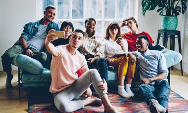 Milenyum çağının neşeli, çok ırklı öğrencilerinin çağdaş dairede boş zamanlarında akıllı telefonlarıyla selfie çekmeleri.