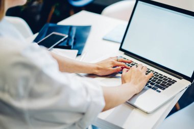 Modern çalışma alanındaki dizüstü bilgisayarları kullanarak yeni bir proje üzerinde çalışırken akıllı telefonlu bir masada oturan isimsiz bir kadın.