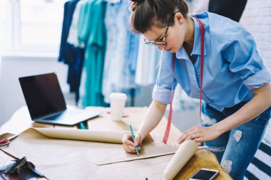 Stüdyoda el işi kağıt ve dizüstü bilgisayarla çalışırken ciddi kadın tasarımcıların çizimlerini ve projelerini yan gözle görmek