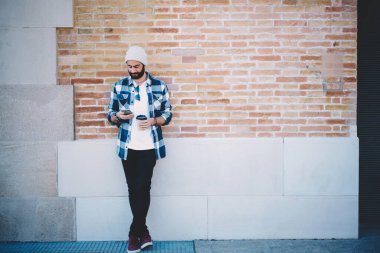 Şehirdeki boş zamanlarında kablosuz internet sayfasına bakmak için 4G 'ye bağlanan modaya uygun giyinmiş erkek blog yazarı