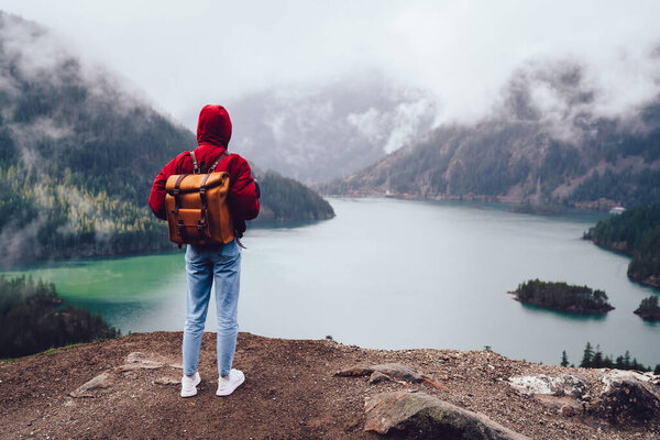 Back view of unrecognizable person standing on rocky coast of fjord with lake against misty sky during autumn season in USA