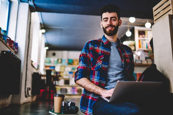 Sıradan giyinmiş yakışıklı sakallı bir gencin portresi. Kameraya gülümserken dizüstü bilgisayar tutuyor..