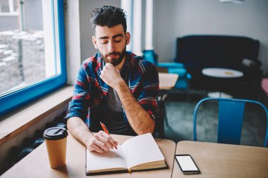 Üniversitede görev çözmeyi düşünürken gidip not defterini açmak. Günlük giyinmiş genç adam yayınlama fikirleri üzerine kafa yoruyor.