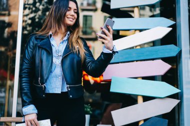 Dişli bir gülümseme içinde, sokakta tabelaların yanında duran ve cep telefonlarını karıştıran mahsul genç bayanlarından.