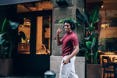 Neşeli erkek turistin yarım boy portresi cep telefonu medya uygulamasını kullanarak şehirde gündüz yürürken pozitif müzik şarkıları dinliyor.