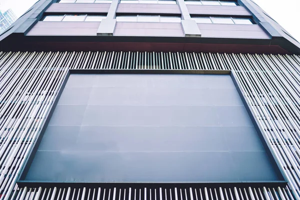 From below of exterior of contemporary geometric building with gray empty panels for banner and balconies in city street at daytime